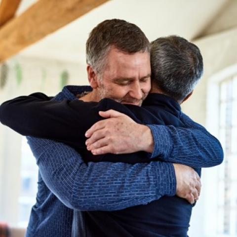 men hugging Two middle-aged men hug in a sunlit house.