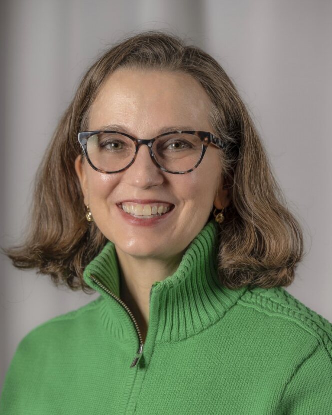 A woman with brown hair and a green sweater smiles at the viewer.