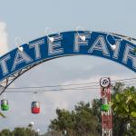 Banner over entrance to Minnesota State Fair reads "State Fair," elevated passenger tram cars in background